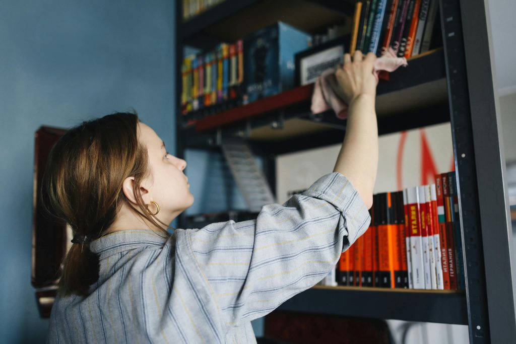A Woman Wiping a Bookshelf with a Cloth